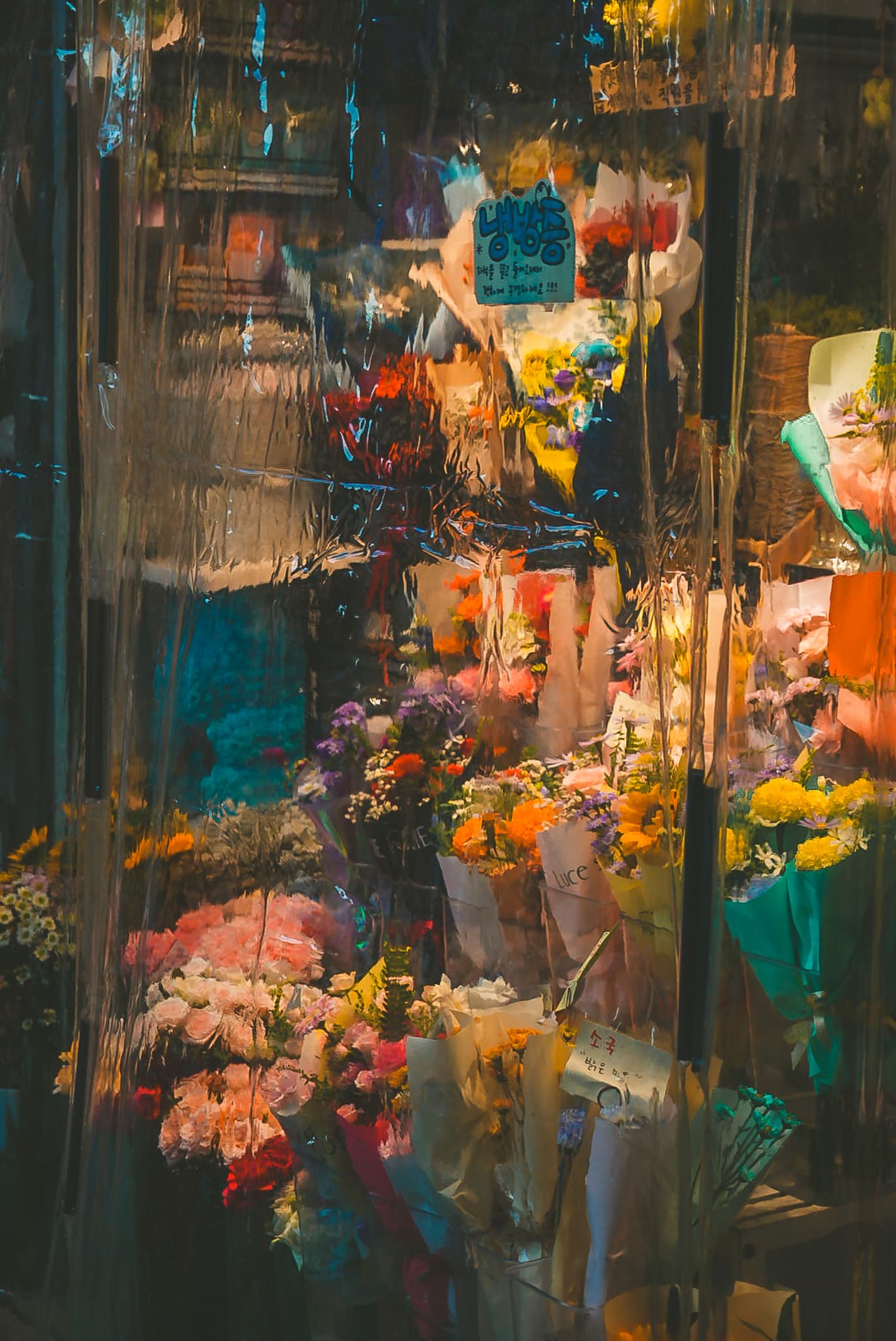 Colorful bouquets displayed behind a translucent plastic curtain, creating a blurred, abstract effect.